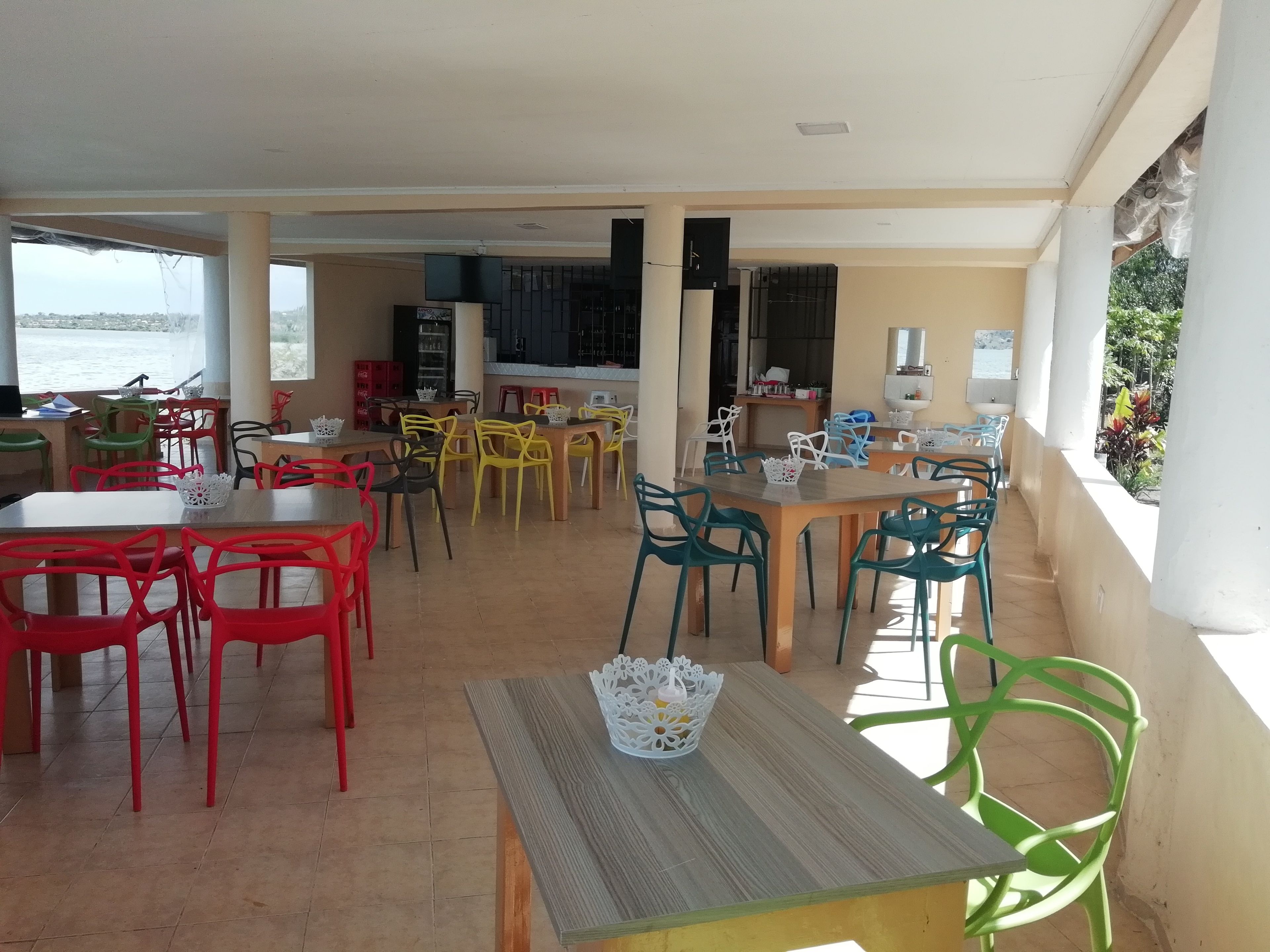 Uma ampla área de refeições com várias mesas e cadeiras, cozinha e vista para o mar.