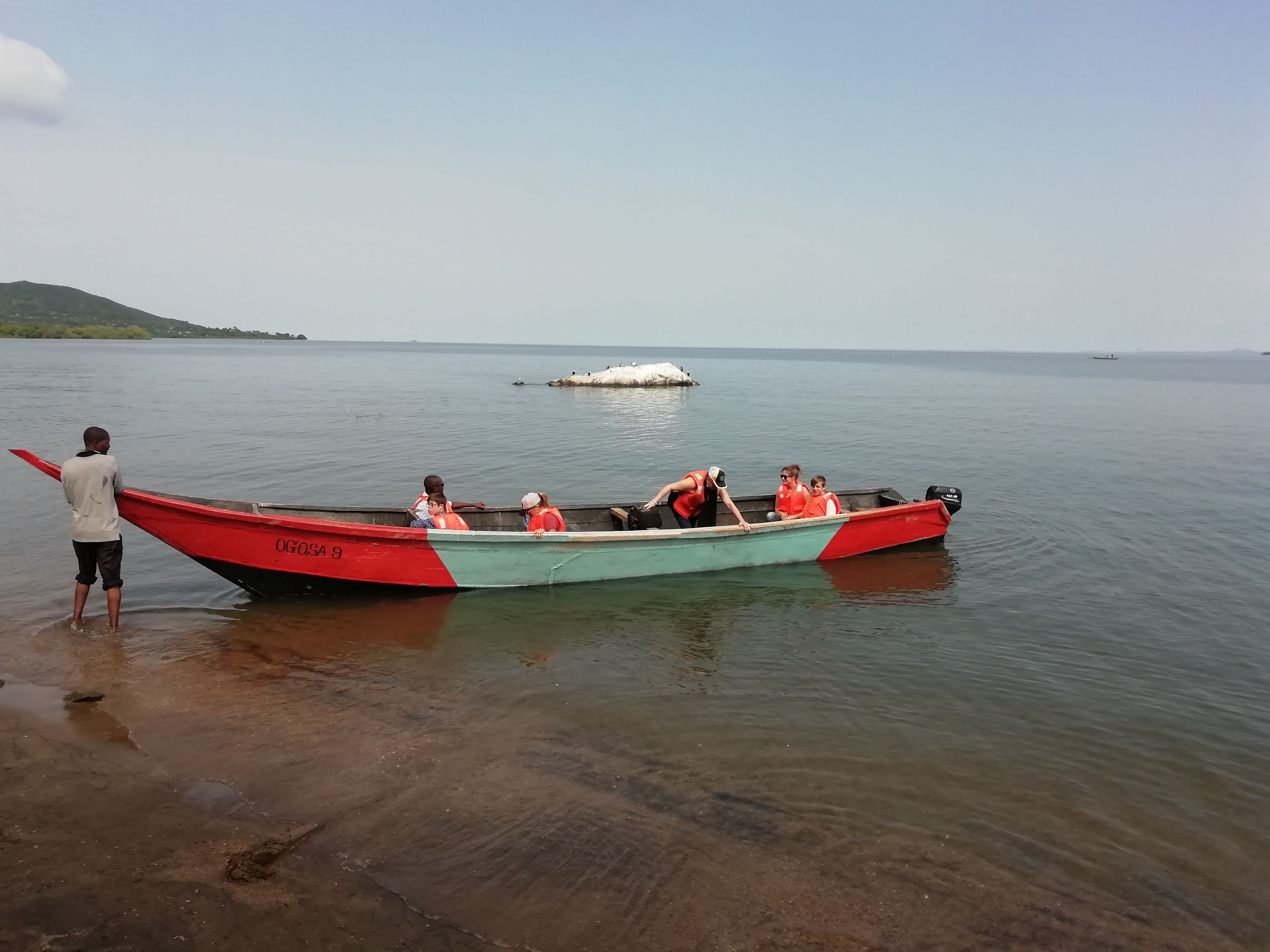 A small boat with people wearing life jackets on a calm body of water.