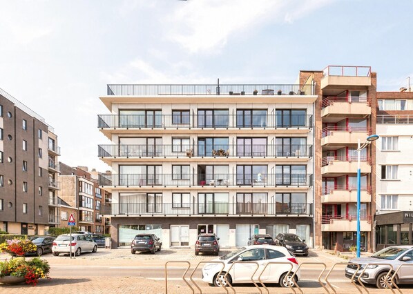 A multi-story residential building with balconies, a parking area with cars, and a street sign indicating a 30m zone.