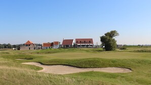 Een golfbaan met bunkers en een clubhuis met een rood dak.