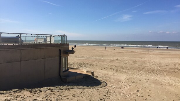 Een strand met een betonnen constructie, mogelijk een bewakerspost, en een heldere lucht.