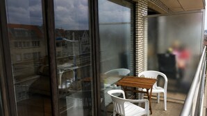 Een balkon met een glazen deur, een houten tafel en twee witte plastic stoelen.