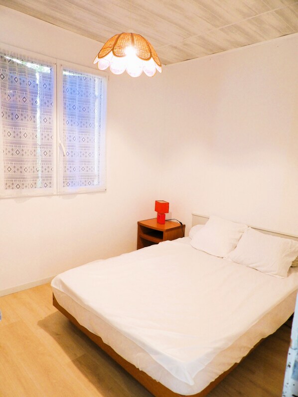 Une chambre à coucher avec un lit, une table de chevet, une lampe et une fenêtre ornée de rideaux à motifs.