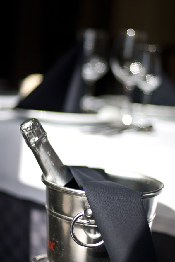 A bottle of champagne in a metal bucket with a black ribbon tied around it, placed on a table with a white tablecloth.