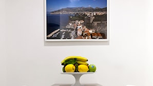 A modern room with a round table, two white chairs, and a framed coastal landscape picture above the table. - Maison Nonna Anna (Sorrento)