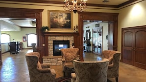 A lobby with a stone fireplace, patterned armchairs, a chandelier, and a large painting above the fireplace.