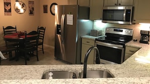 A kitchen with a stainless steel refrigerator, a microwave, an oven, and a toaster. There is a sink with a faucet, and a dining table with chairs.