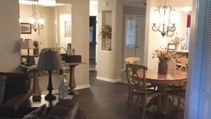 A living room with a brown leather couch, a dining table with chairs, and a chandelier.