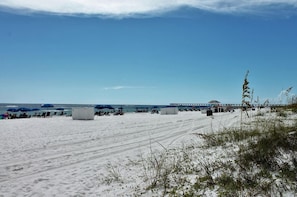 A beach with white sand, umbrellas, and lounge chairs.