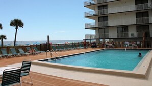 A pool area with lounge chairs and a view of the ocean.