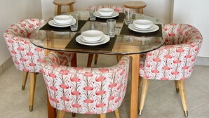 A dining area with a glass-top table, floral-patterned chairs, and a view of the kitchen in the background.
