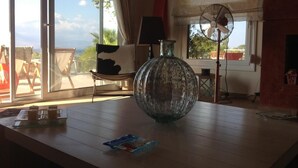 Une pièce avec une grande fenêtre, un ventilateur, un vase en verre et une table sur laquelle se trouve un plateau.