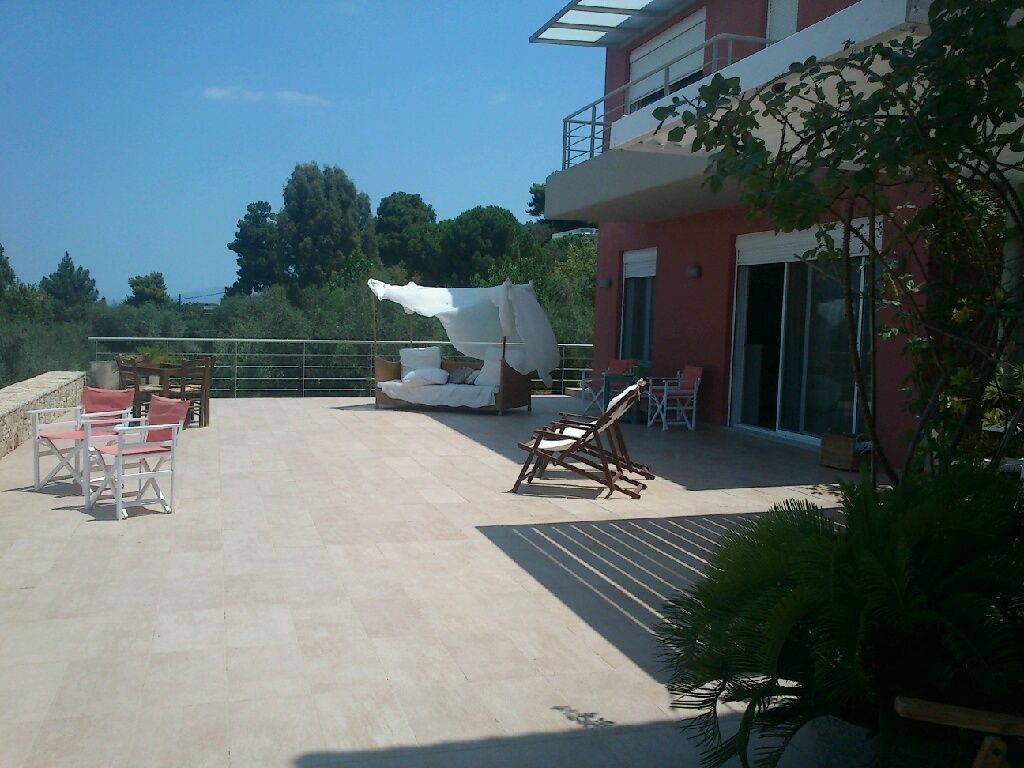 A rooftop patio with outdoor seating, a white chair, and a red building in the background.