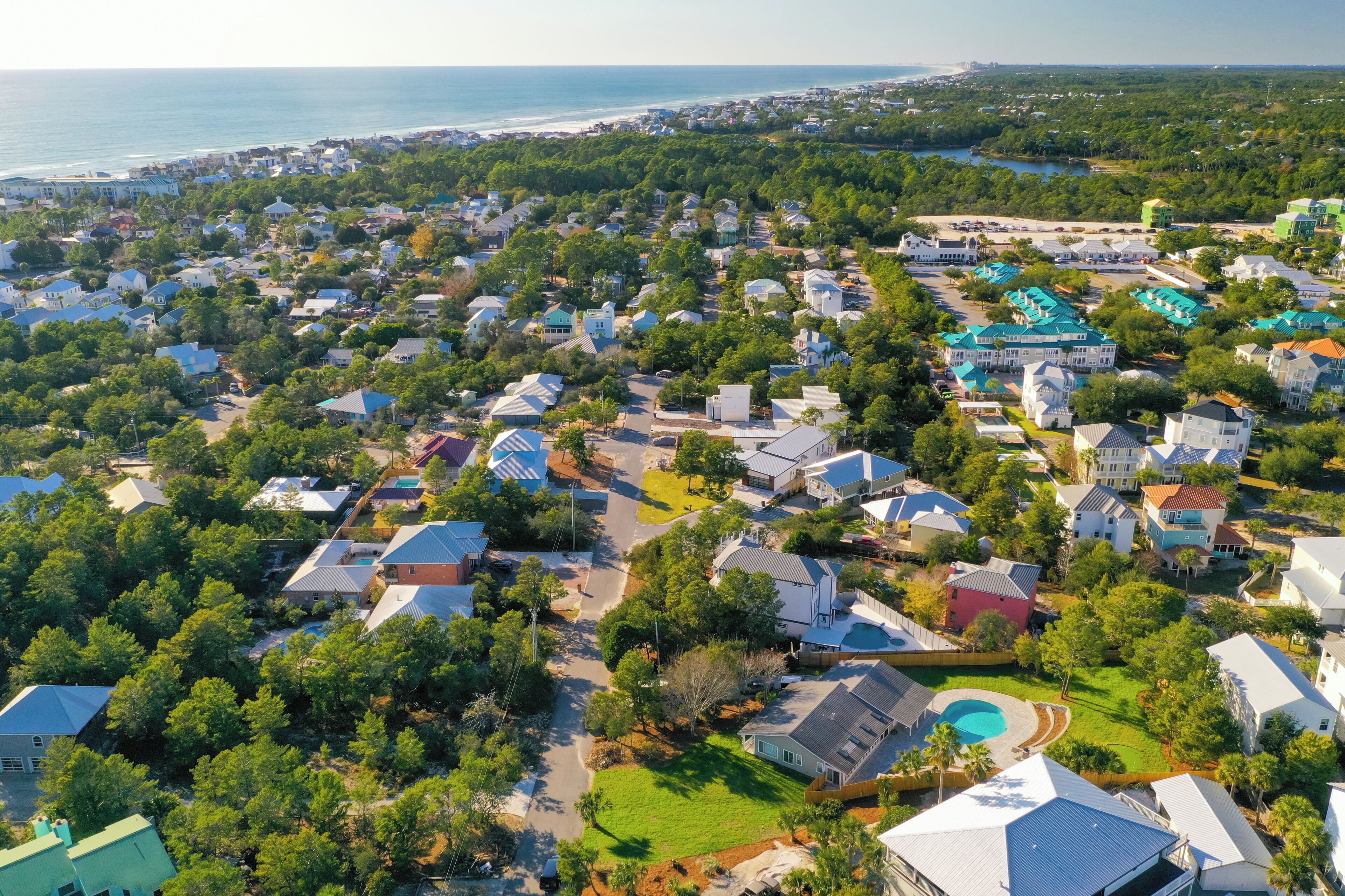 An aerial view of a residential area with houses, a swimming pool, and a large body of water in the background.