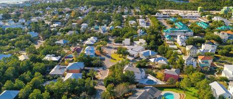 An aerial view of a residential area with houses, a swimming pool, and a large body of water in the background.