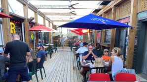 Un espace extérieur aménagé pour les repas, avec des tables et des chaises en bois, des parasols et une terrasse en bois.