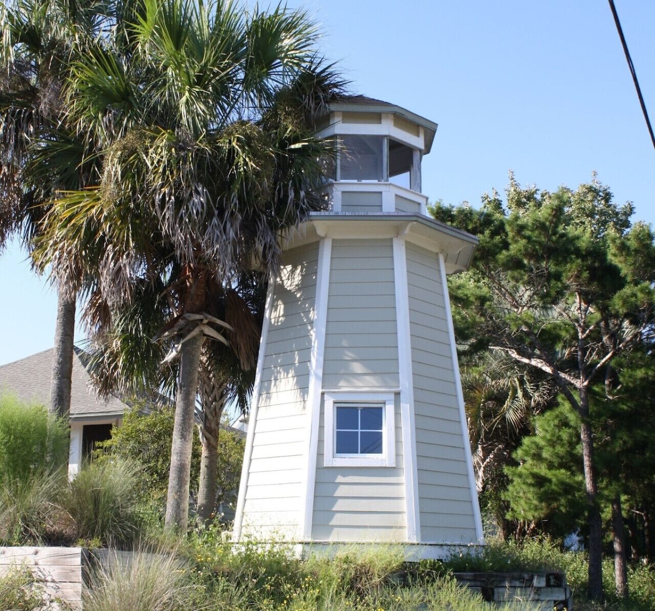 A white lighthouse with a small window, surrounded by palm trees and other vegetation.