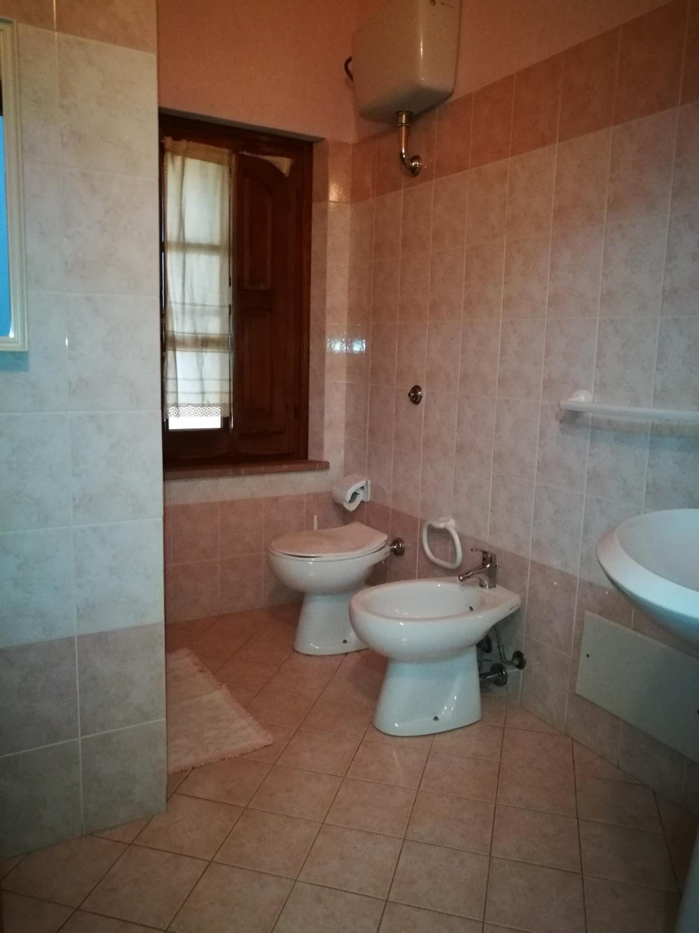 Un baño con dos inodoros, un lavabo y una ventana con cortinas.