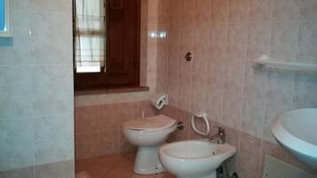 Un baño con dos inodoros, un lavabo y una ventana con cortinas.