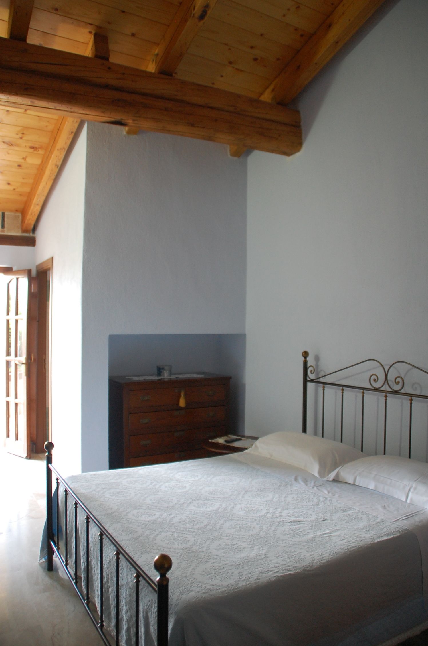 A bedroom with a wooden ceiling, a bed with a metal frame, a dresser, and a door.