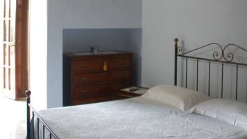 A bedroom with a wooden ceiling, a bed with a metal frame, a dresser, and a door.