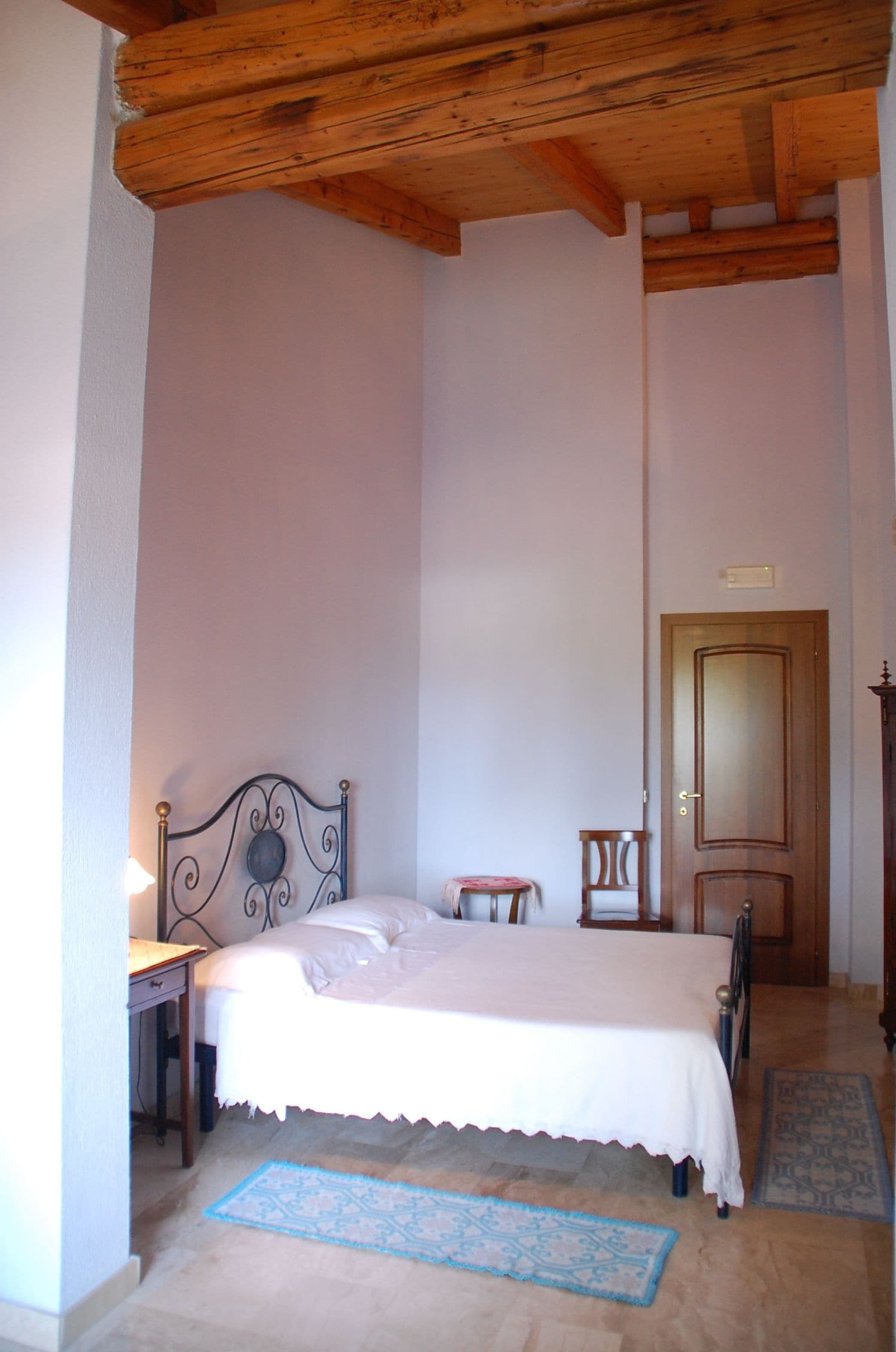 Ein Schlafzimmer mit einem Einzelbett, Holzboden, einem kleinen Tisch, einem Stuhl und einer Tür.