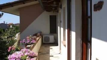 Un corridoio esterno coperto con pavimento in pietra, soffitto in legno e una porta sulla destra.