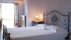 A bedroom with a bed, a nightstand, a lamp, and a window with a view. - Sa Crannaccia (Cabras)