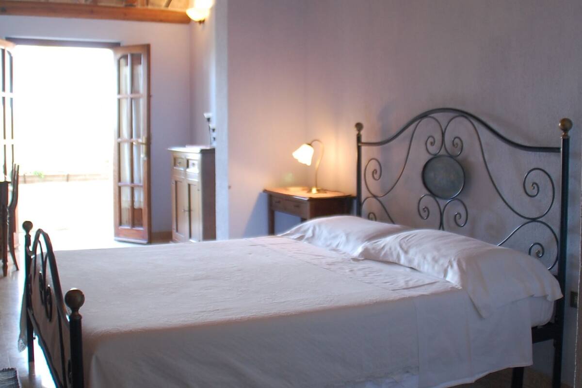A bedroom with a bed, a nightstand, a lamp, and a window with a view.