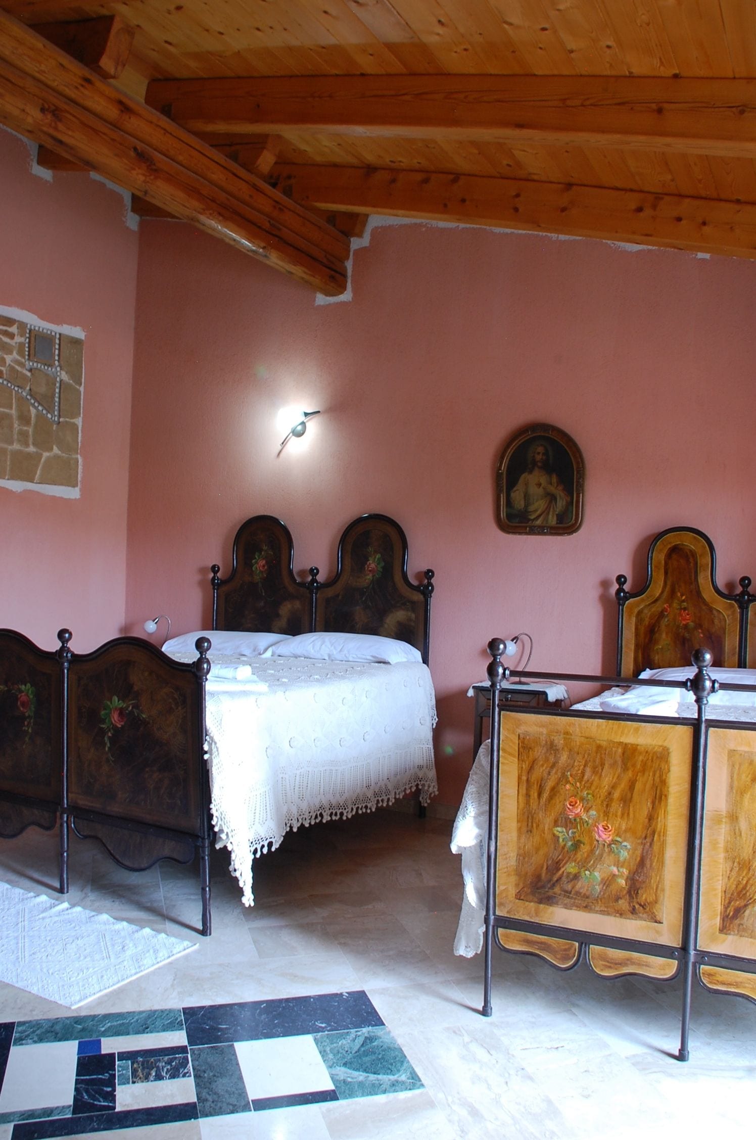 A bedroom with two wooden beds, a stone wall, a wooden ceiling, and a tiled floor.