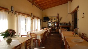 A restaurant with wooden beams, tables with yellow tablecloths, and a bar area with bottles. - Sa Crannaccia (Cabras)