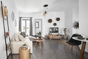 A modern living room with a sofa, coffee table, and dining area. - Pnoi Luxury Suites (Santorini)