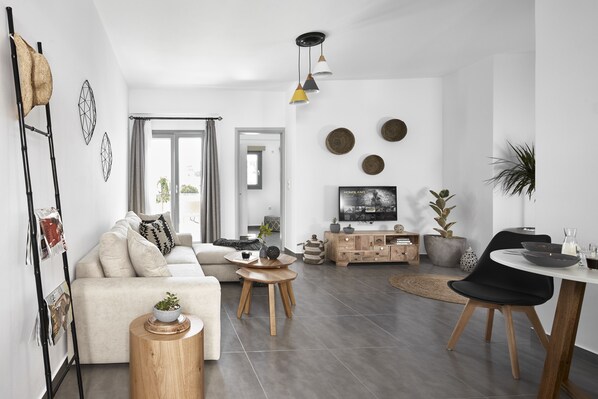 A modern living room with a sofa, coffee table, and dining area. - Pnoi Luxury Suites (Santorini)