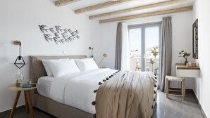 A bedroom with a bed, bedside table, lamp, and a view of the outside. - Pnoi Luxury Suites (Santorini)