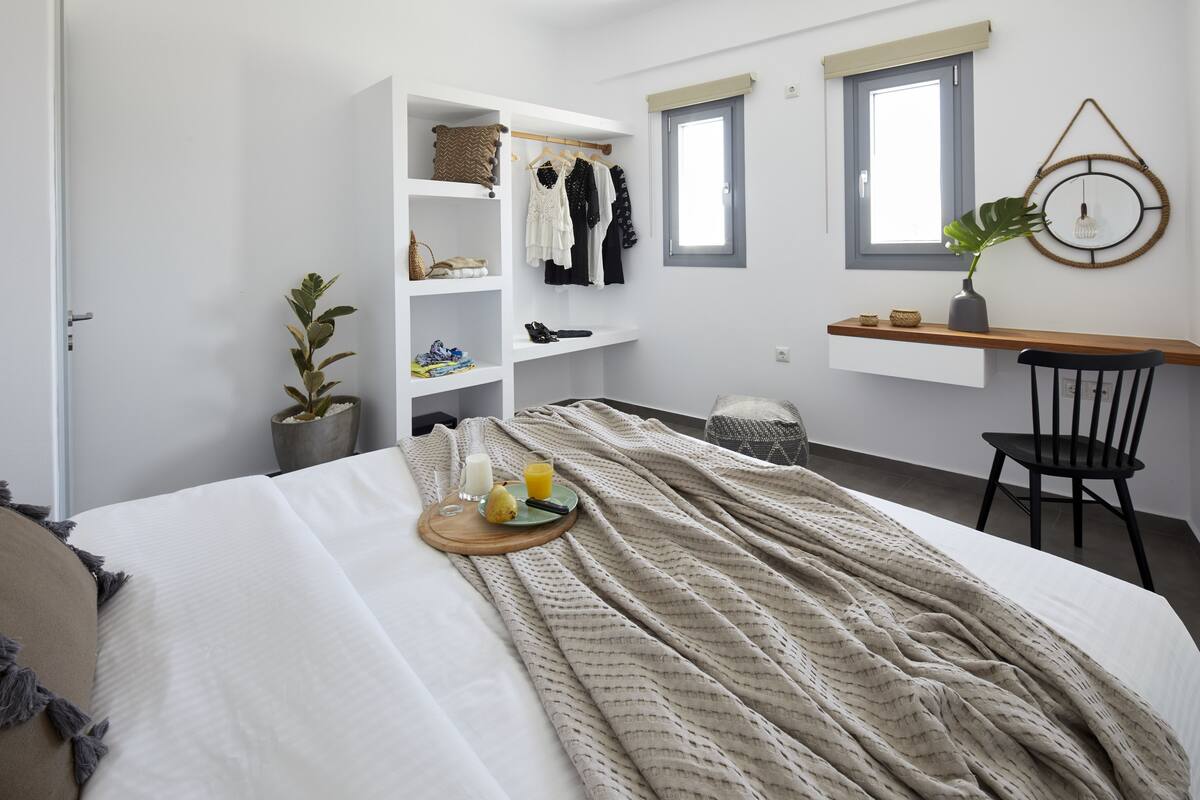A bedroom with a bed, bedside table, chair, wardrobe, and windows.