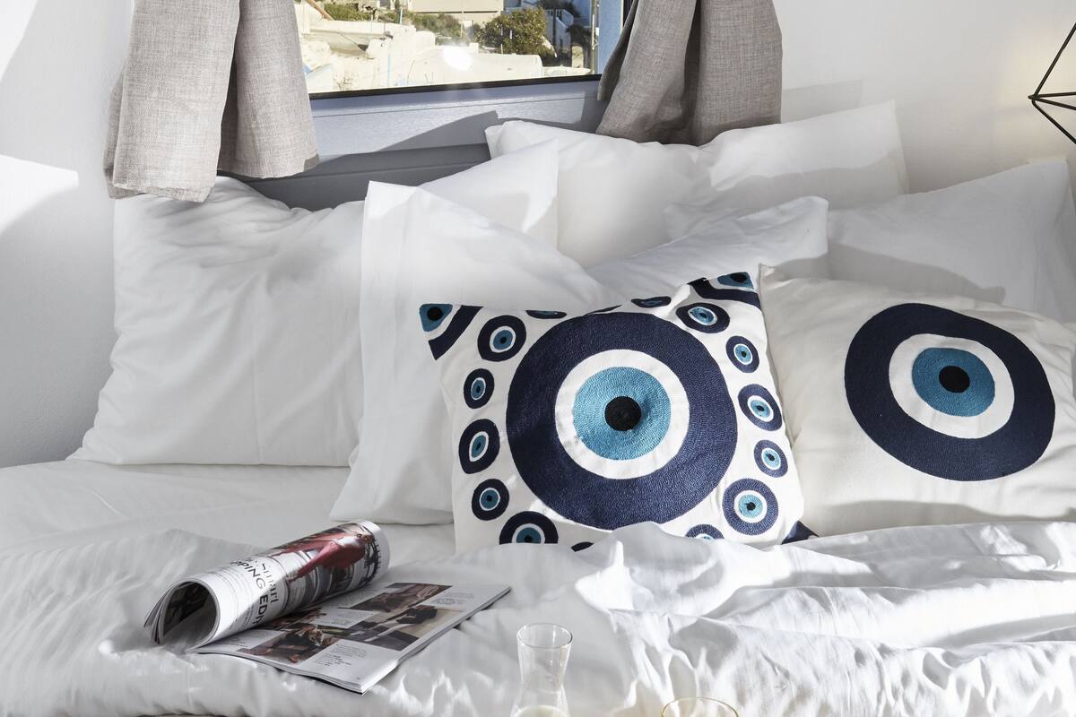 A hotel room with a bed, pillows, a tray with breakfast items, and a view of a cityscape through a window.