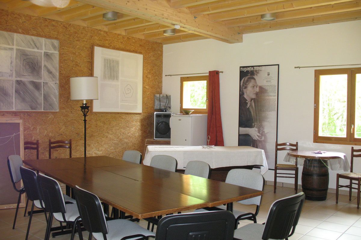 A dining area with a long wooden table, several chairs, a small kitchen area with a stove, and a poster on the wall.