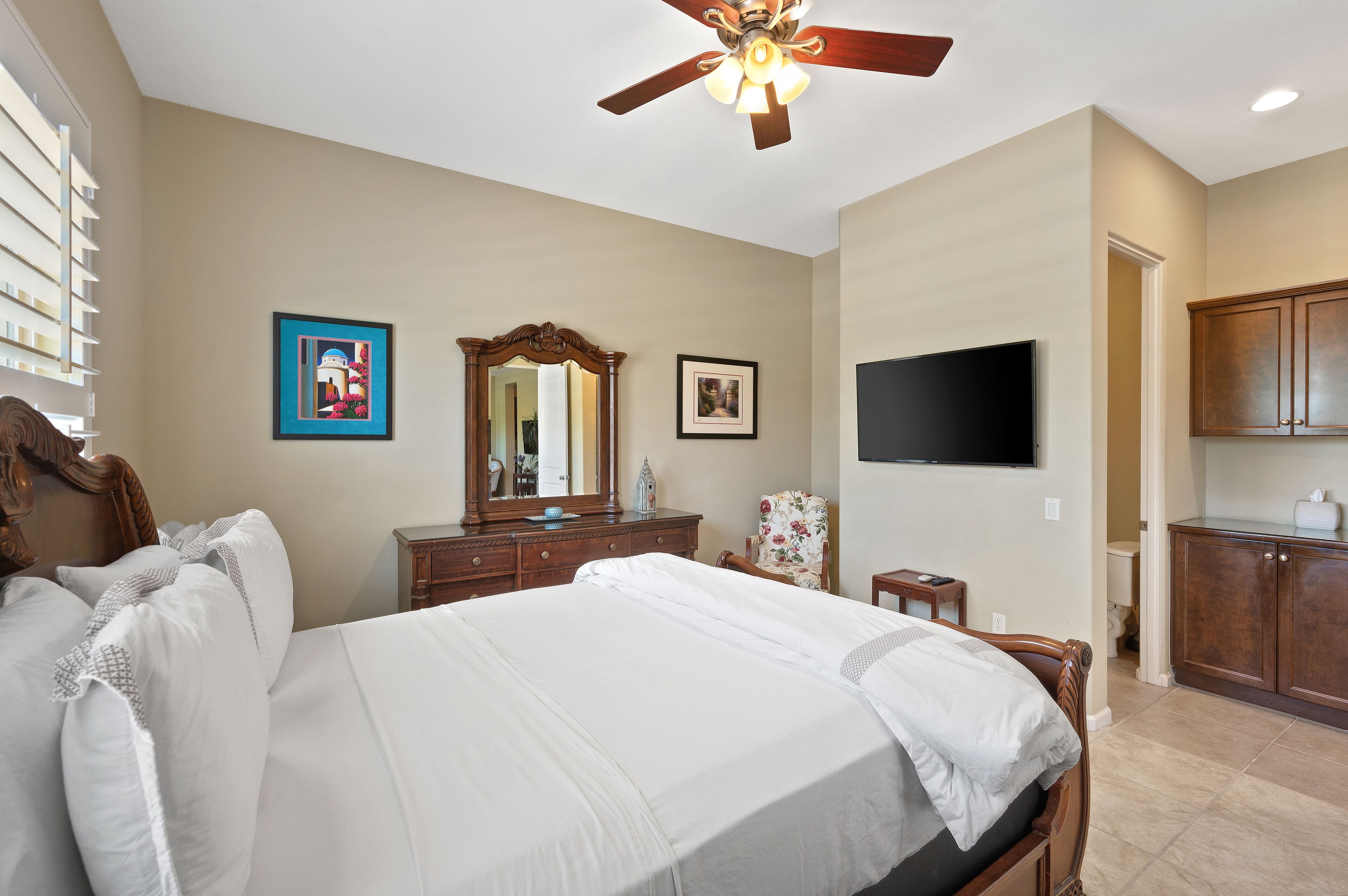 Une chambre à coucher avec un grand lit, une commode, un miroir, une télévision et un ventilateur de plafond.