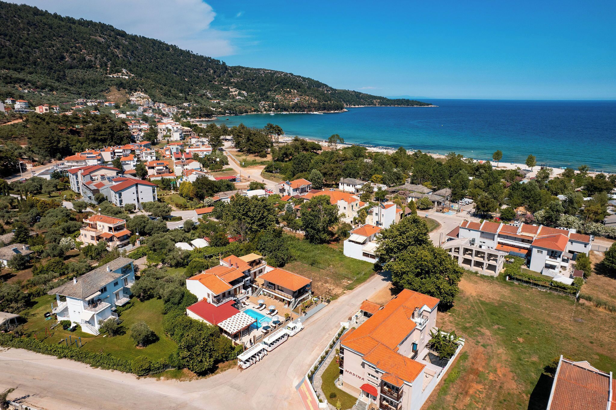 Vista aérea de una zona residencial costera con casas, una playa y un cielo azul despejado.