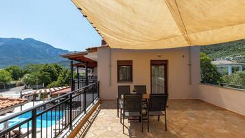 Un balcón con mesa y sillas, una piscina y vistas a las montañas.