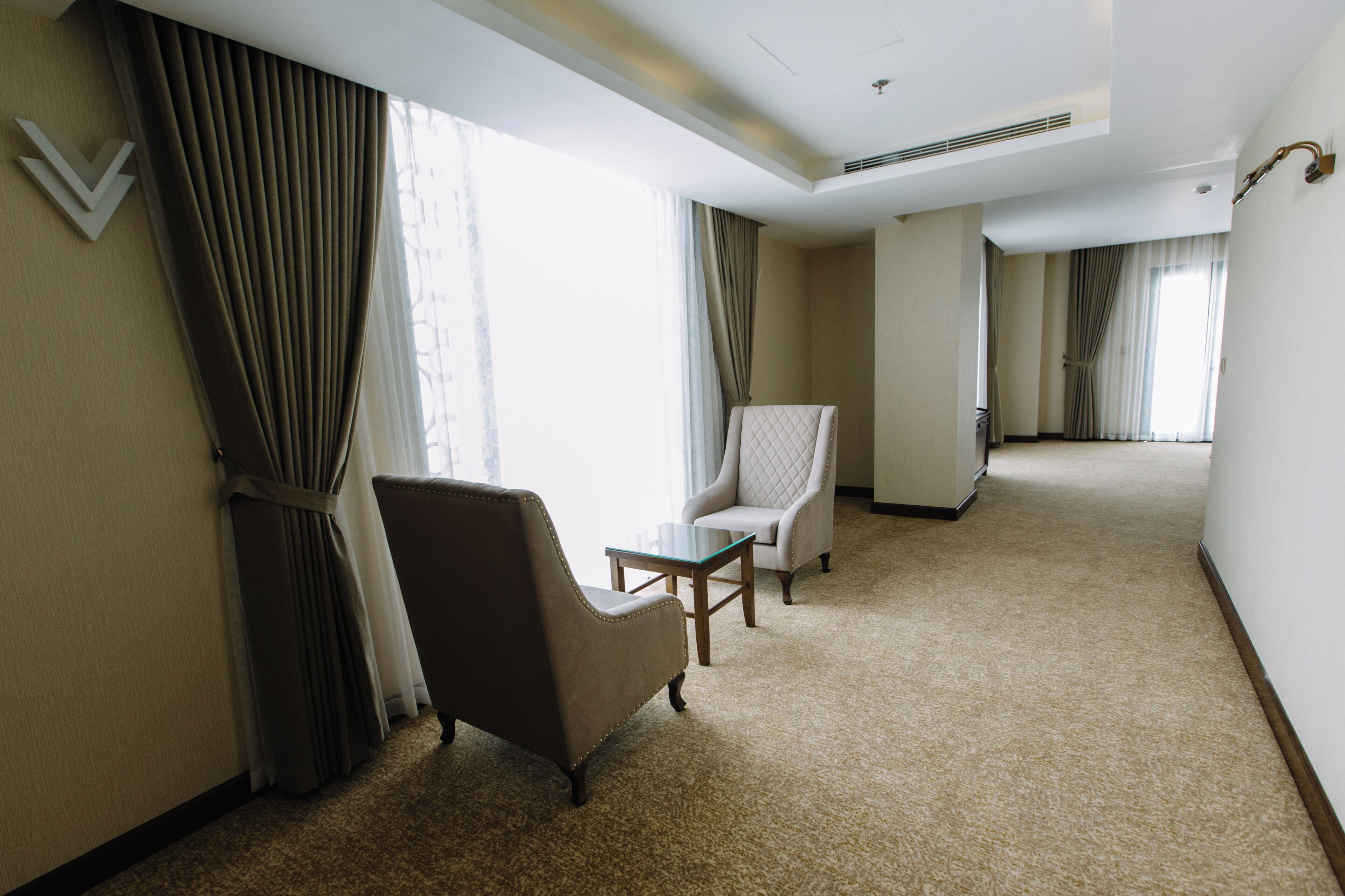 Habitación de hotel con un ventanal grande, una silla, una mesita y suelo alfombrado.