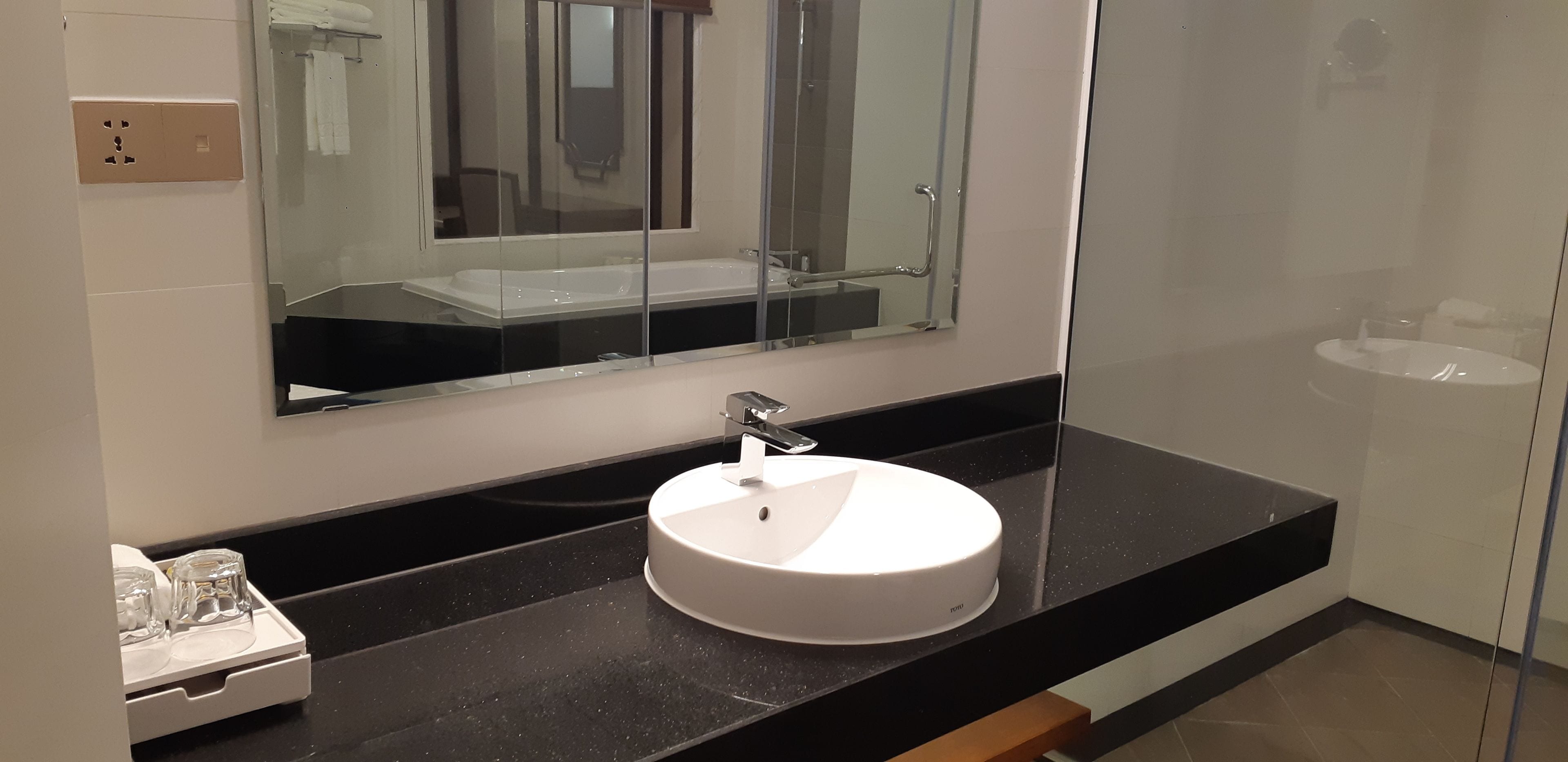 Uma casa de banho moderna com uma lavatório redondo, um espelho grande e um compartimento de chuveiro em vidro.