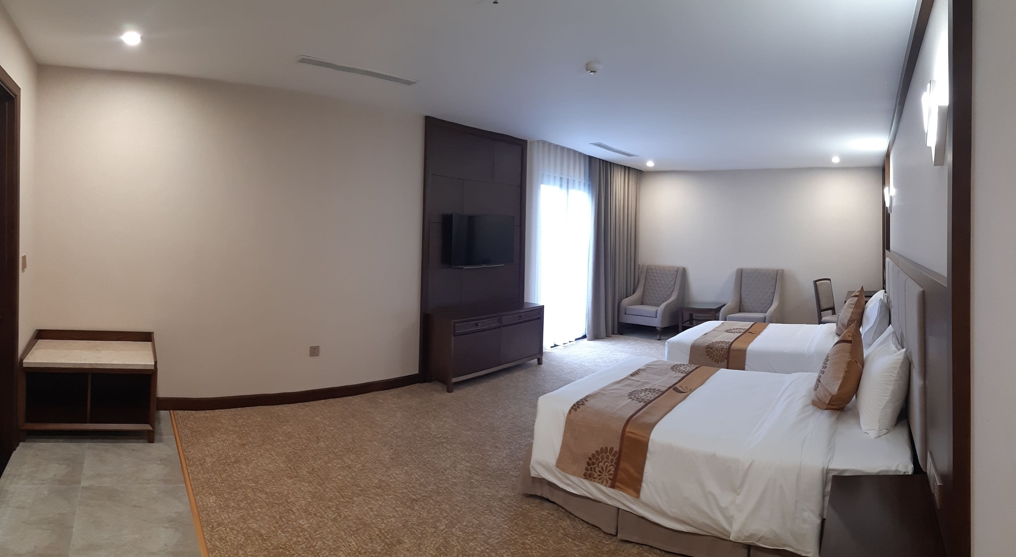 Habitación de hotel con dos camas, televisión, zona de estar con sillas y una mesita.