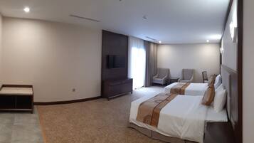 Habitación de hotel con dos camas, televisión, zona de estar con sillas y una mesita.