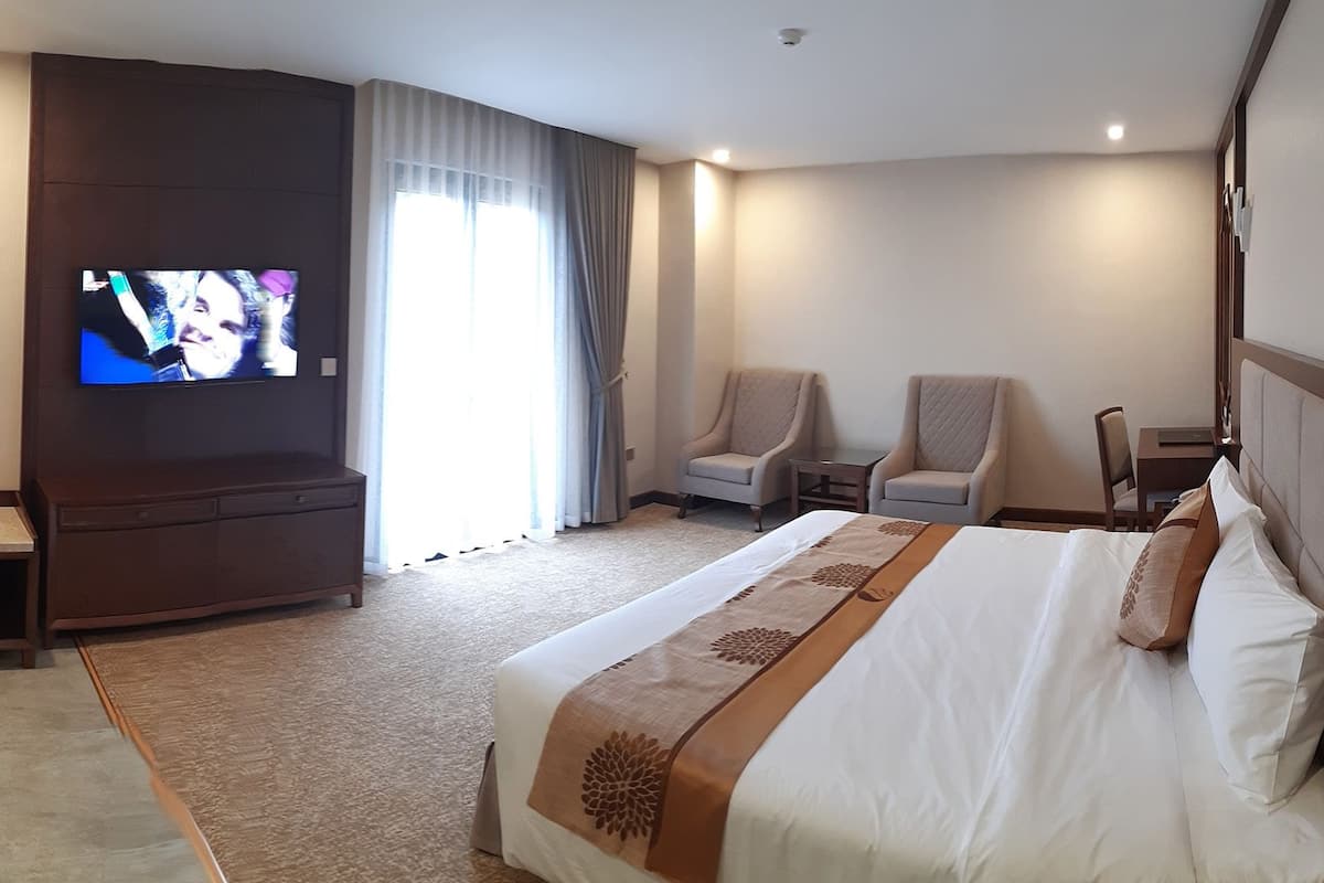 A hotel room with a large bed, a TV mounted on the wall, two armchairs, a small table, and a desk.