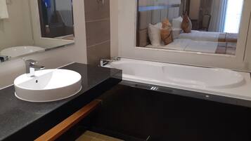 A modern bathroom with a round sink, a large bathtub, and a mirror above the sink.