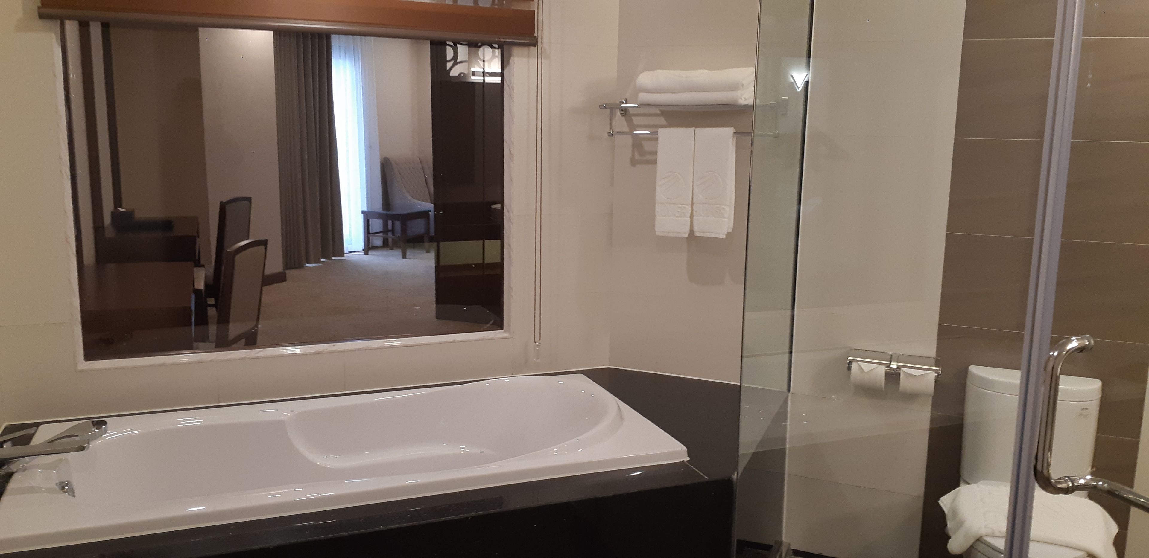 Een moderne badkamer met een groot bad, een douchecabine van glas en een zichtbare eethoek op de achtergrond.