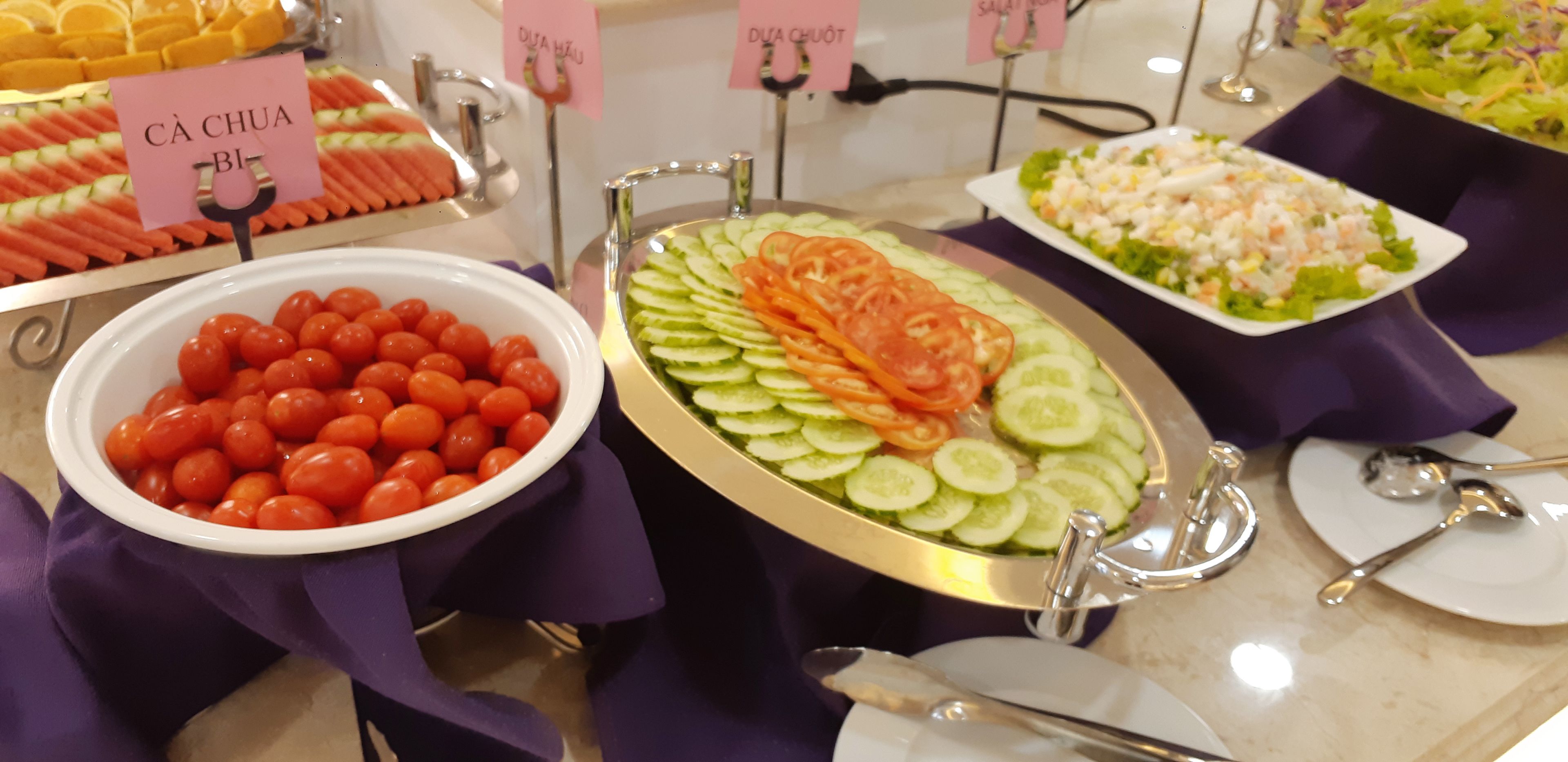 A buffet with various food options including a bowl of cherry tomatoes, a cucumber salad, and a salad with shrimp.