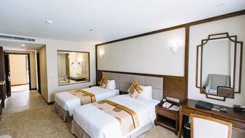 Habitación de hotel con dos camas, un escritorio, una silla, un espejo y un baño visible al fondo.