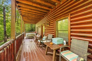 Enjoy a peaceful retreat on the covered porch with a table, chairs, and bench, surrounded by the serene woods.